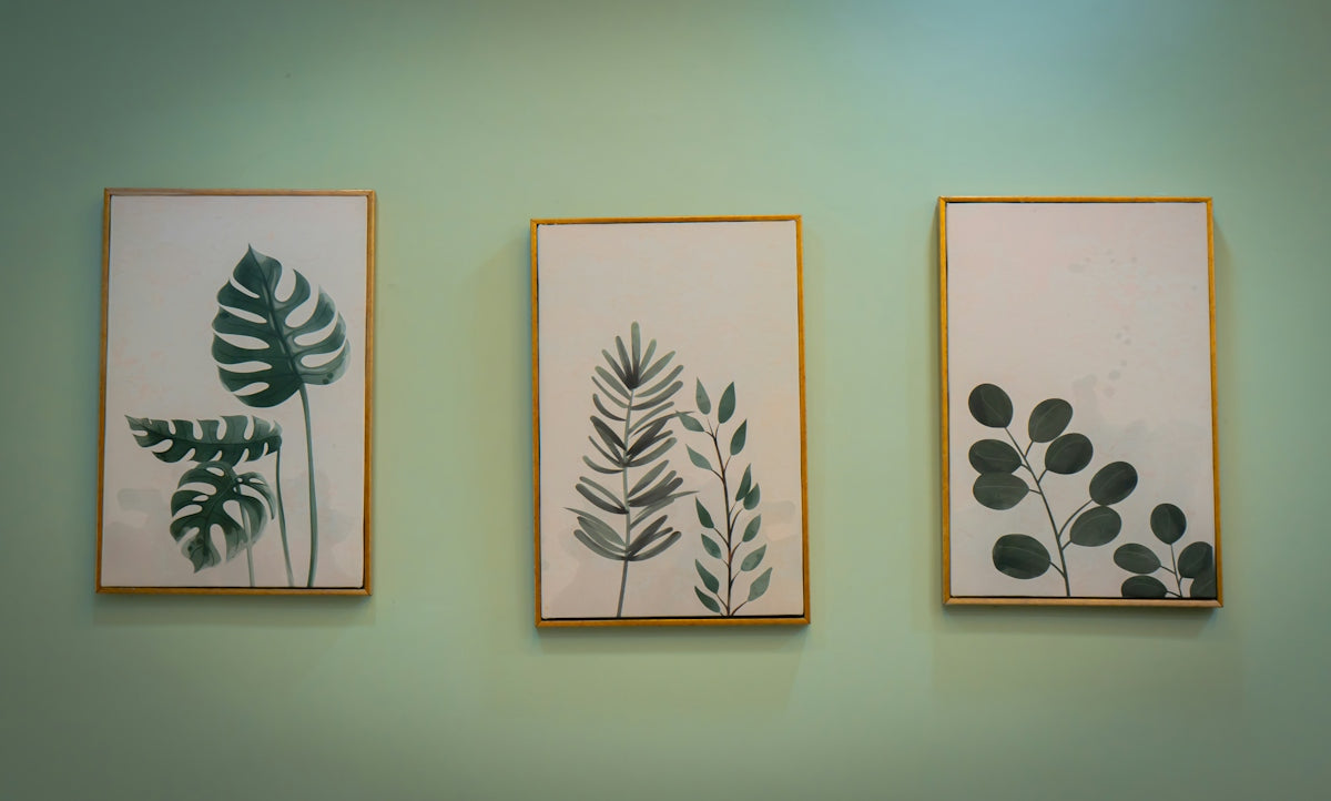 Three framed botanical prints with green leaves on a light green wall